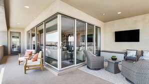 Een moderne woonkamer met een glazen scheidingswand, comfortabele zithoeken, een flatscreen televisie en een klein bijzettafeltje met een plant.