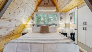 Un dormitorio con techo inclinado, una cama con ropa de cama blanca, una ventana con persianas y un armario empotrado.