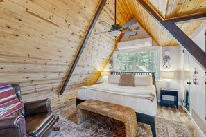 A cozy bedroom with a sloped ceiling, a bed with a headboard, a bench, a chair, and a small bedside table. - Updated Cabin w/ hot tub, wrap around deck, yard, & loft - 1 dog ok (Munds Park)