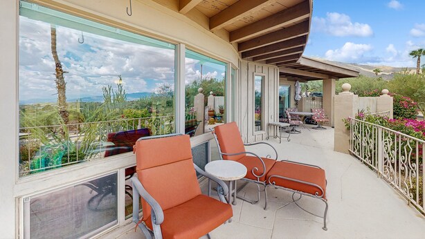 Ein Balkon mit orangefarbenen Stühlen und einem Tisch, große Fenster mit Blick auf Wüste und Berge sowie ein weißes Geländer.