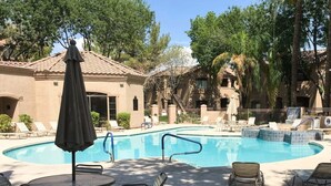 Una piscina con sillas de descanso y sombrillas, rodeada de edificios con techo de tejas.