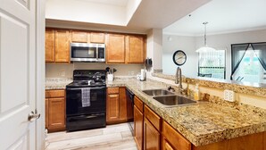 Una cocina con armarios de madera, un lavamanos de acero inoxidable, encimeras de granito, una estufa negra y un microondas.