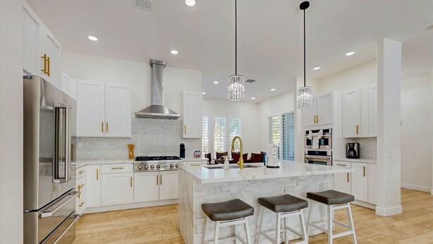 A modern kitchen with white cabinetry, a central island with stools, stainless steel appliances, and pendant lighting.