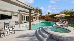 A modern outdoor pool area with a hot tub, lounge chairs, and a covered patio.