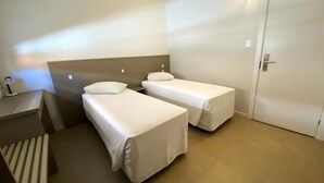 Habitación de hotel con dos camas individuales, una mesita de noche con lámpara y una puerta.