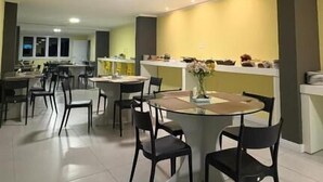 Un comedor amplio con varias mesas y sillas, una zona de cocina al fondo y una pared de acento amarilla.