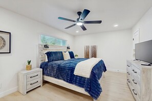 Ein Schlafzimmer mit Bett, Nachttisch, Kommode, Deckenventilator und Fernseher.