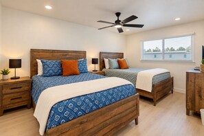Une chambre avec deux lits, des têtes de lit en bois, des lampes de chevet, un ventilateur de plafond et une fenêtre avec des stores.