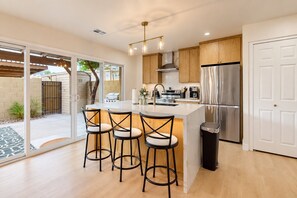 A modern kitchen with a central island, bar stools, stainless steel appliances, and a sliding glass door leading to a patio. - Modern Comfort & Desert Fun—A Chic Two-Story Home Base Minutes From Everything. (Scottsdale)