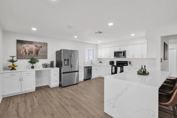 A modern kitchen with white cabinetry, stainless steel appliances, and a marble island. - Newly renovated, this home offers a modern retreat with amenities (Tempe)