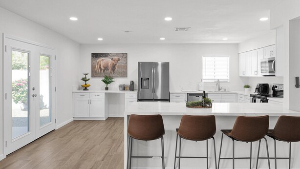 Een moderne keuken met witte kasten, roestvrijstalen apparatuur en een centraal eiland met barstoelen.