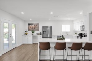A modern kitchen with white cabinetry, stainless steel appliances, and a central island with bar stools. - Newly renovated, this home offers a modern retreat with amenities (Tempe)