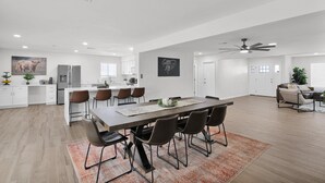 Een ruime keuken met een centraal eiland, een eetgedeelte met een lange tafel en stoelen, en een zithoek met een bank en salontafel.