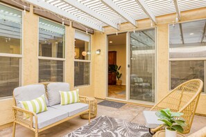 A covered patio area with a sofa, a wicker chair, and a potted plant.