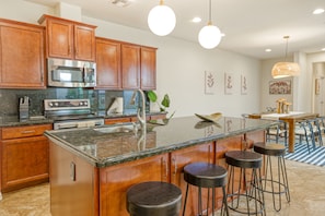 A modern kitchen with wooden cabinets, stainless steel appliances, a granite countertop, and bar stools. - Quaint home walking distance to Superbowl with patio, AC, W/D & pool access (Glendale)