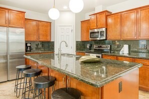 A kitchen with wooden cabinets, a stainless steel refrigerator, a microwave, and a granite countertop.