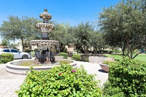 A multi-tiered fountain surrounded by lush greenery and a paved walkway.