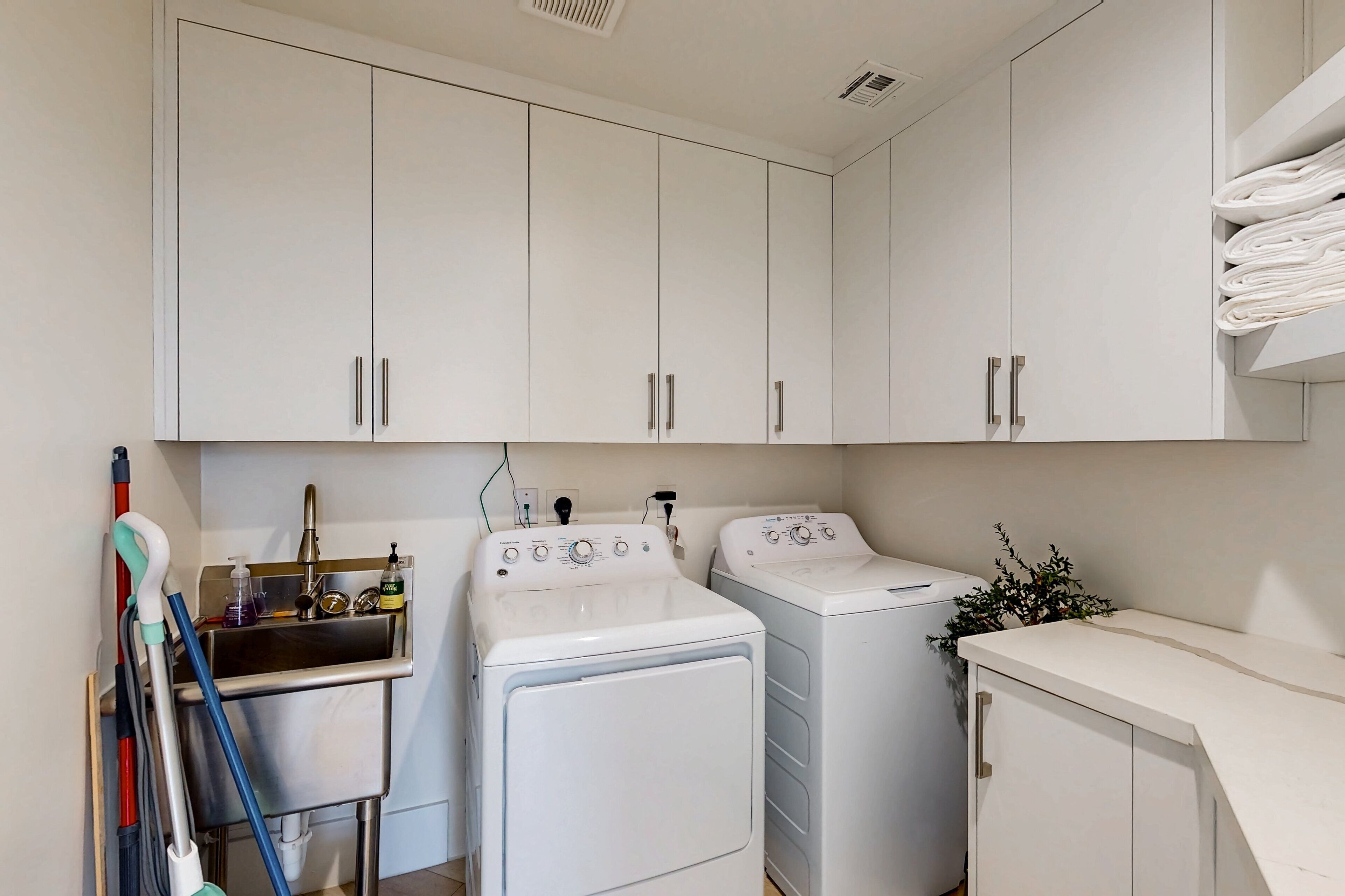 A laundry area with two white washing machines, a sink with a faucet, and a mop leaning against the wall.