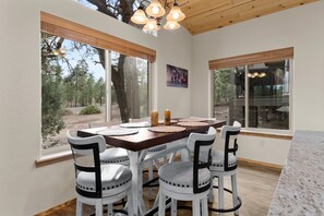 A dining area with a wooden table, white chairs, and a view of trees through large windows. - Luxury home with patio, fireplace, BBQ grill, golf nearby (Show Low)