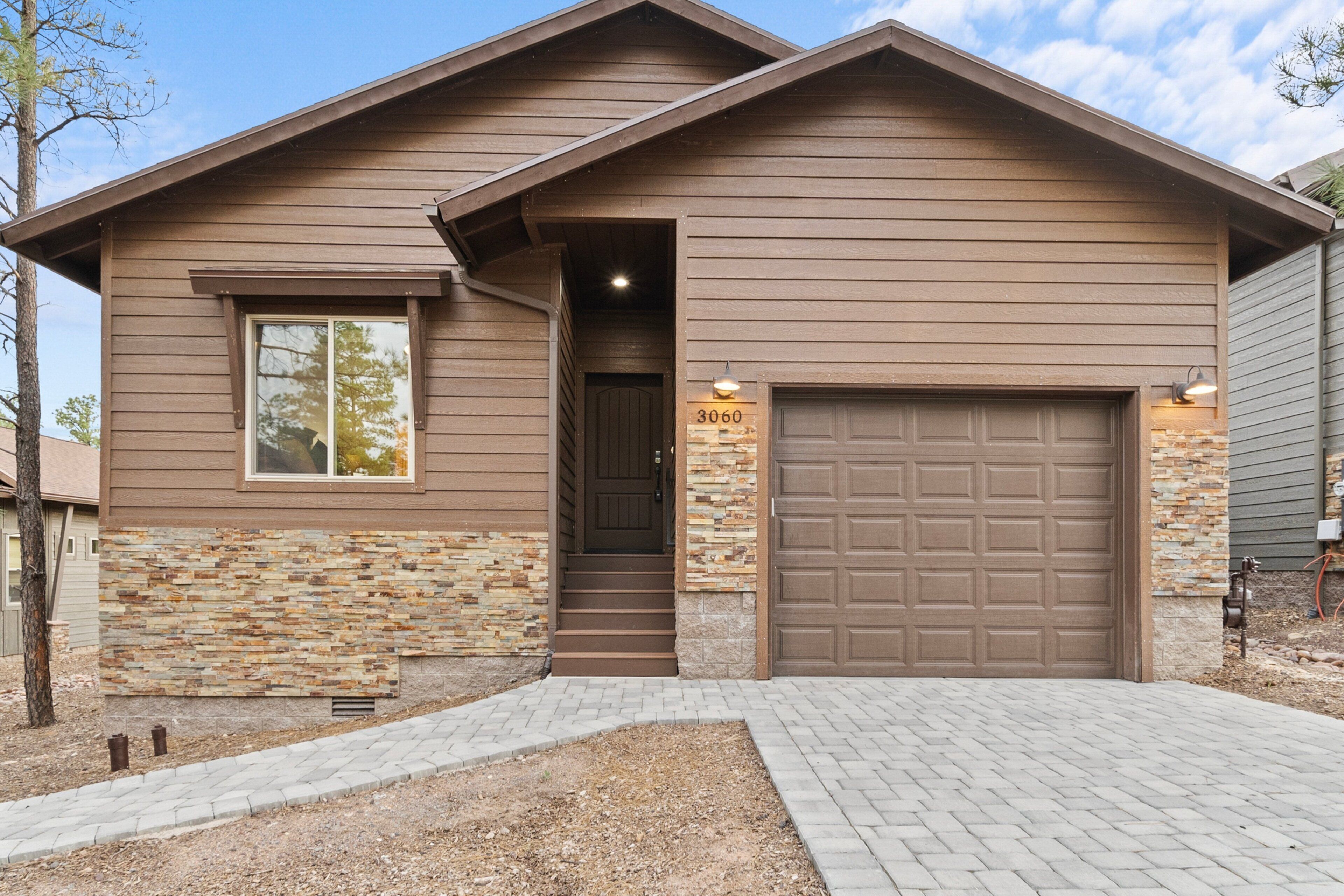 A two-story house with a stone facade, a brown garage door, and a number '3060' sign.