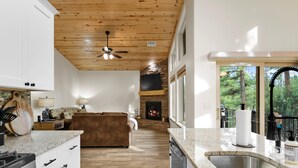 Un'ampia cucina con soffitto in legno, un camino in pietra e una grande finestra vista foresta.