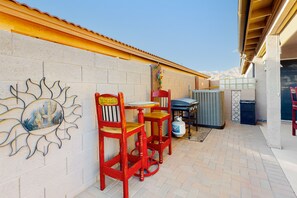 Un patio con suelo de ladrillo, sillas de madera roja, una mesita y un adorno en la pared.