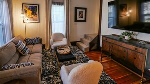 A living room with a sofa, armchair, coffee table, and a TV on a wooden cabinet. - Hot Tub in Downtown Blue Beauty - Walk to Lake, Sherman & Events (Coeur d`Alene)