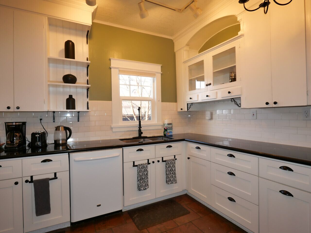 A kitchen with white cabinets, a black countertop, and a window with white trim.
