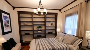 A neatly arranged bedroom with a large bed, a bedside table, a chair, a bookshelf, and a chandelier. - Hot Tub in Downtown Blue Beauty - Walk to Lake, Sherman & Events (Coeur d`Alene)