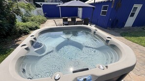Un jacuzzi dans un jardin, avec une maison bleue en arrière-plan.
