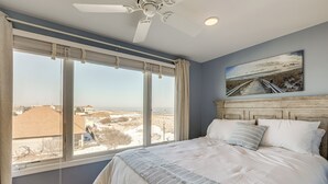 Une chambre avec un grand lit, un ventilateur de plafond, une vue sur la plage et un tableau accroché au mur.