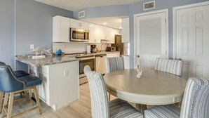 Une cuisine moderne avec des armoires blanches, un four à micro-ondes encastré et un coin repas avec des chaises à rayures.