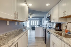 A modern kitchen with white cabinets, granite countertops, and a central island. - Oceanside Retreat in Mantoloking: Walk to Beach! (Mantoloking)