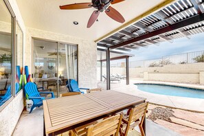 An outdoor patio with a pool, wooden table, chairs, and a ceiling fan. - Dreamy desert gem with private pool, firepit, grill, lanai & AC (Goodyear)