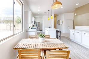 A modern kitchen with white cabinets, a wooden dining table, and pendant lights. - Dreamy desert gem with private pool, firepit, grill, lanai & AC (Goodyear)