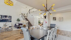 Un amplio salón con una mesa de comedor de madera oscura, sillas blancas y una escalera que sube a un piso superior.