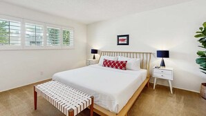 Quarto com cama, mesas de cabeceira, um banco e uma janela com persianas.