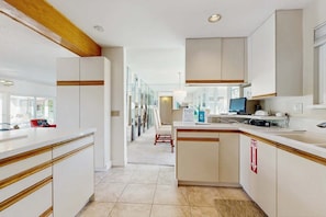A modern kitchen with white cabinetry, a central island, and a view into the dining area. - Stylish Dog-Friendly Retreat W/ High-Speed WiFi, Pool & Spa, & Pool Table (Palm Springs)