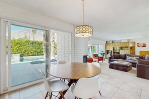 A modern living room with a dining area, large windows, and a view of a pool. - Stylish Dog-Friendly Retreat W/ High-Speed WiFi, Pool & Spa, & Pool Table (Palm Springs)