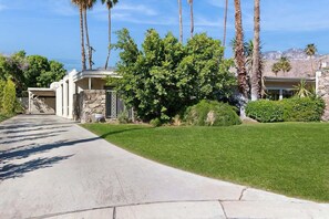 A residential property with a paved driveway, a well-maintained lawn, and a stone wall. - Stylish Dog-Friendly Retreat W/ High-Speed WiFi, Pool & Spa, & Pool Table (Palm Springs)