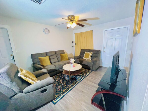 A living room with a sofa, armchair, coffee table, and a ceiling fan.