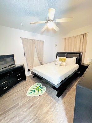 A bedroom with a bed, a ceiling fan, a TV, and a desk.