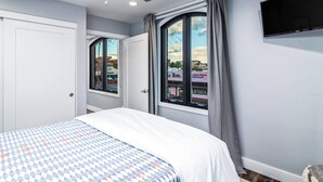 Een slaapkamer met een bed, een plafondventilator, een aan de muur bevestigde televisie en een raam met gordijnen.