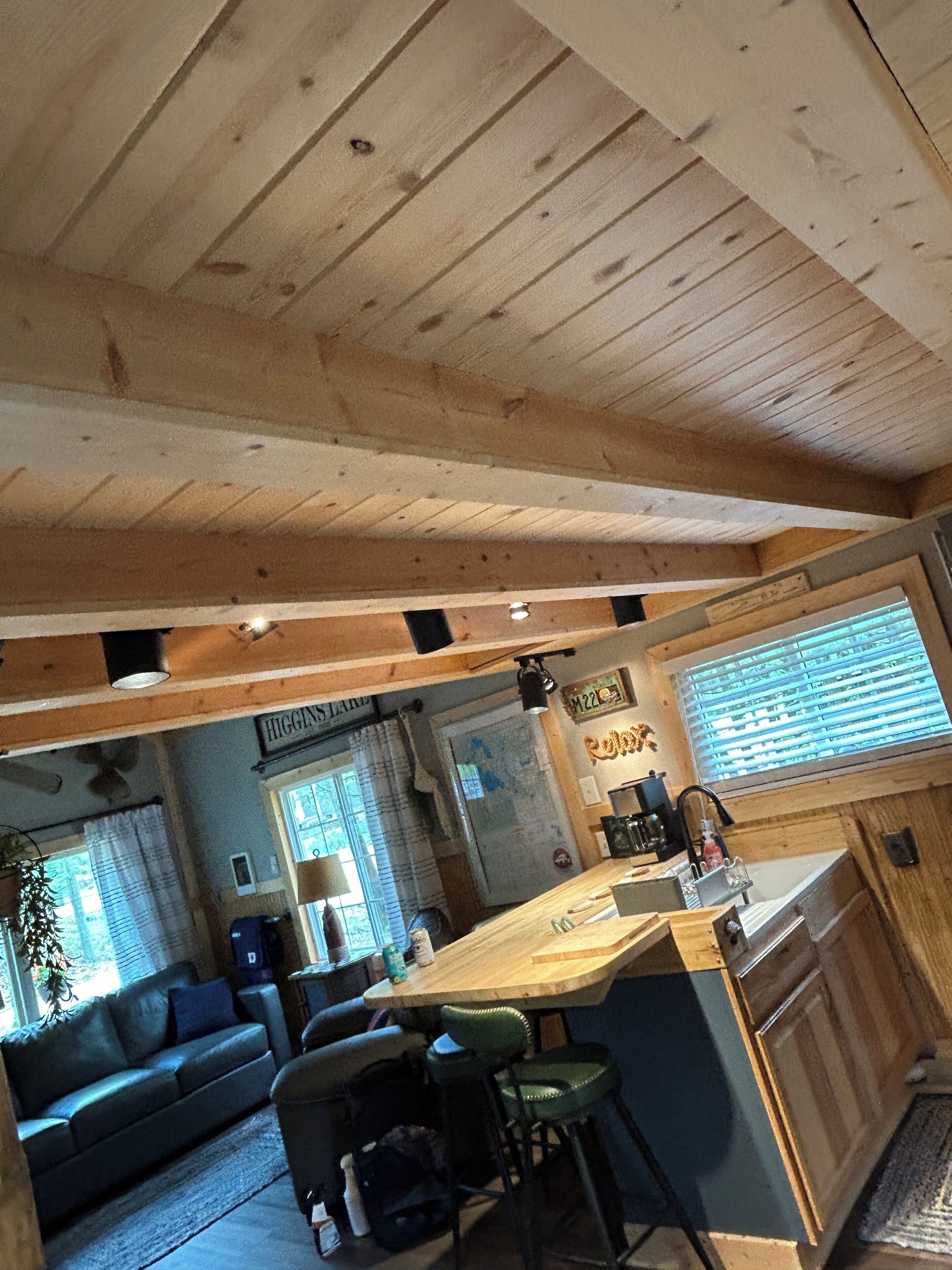 L’intérieur chaleureux d’un chalet avec un plafond en bois, un coin cuisine doté d’un bar, un canapé et une table à manger.