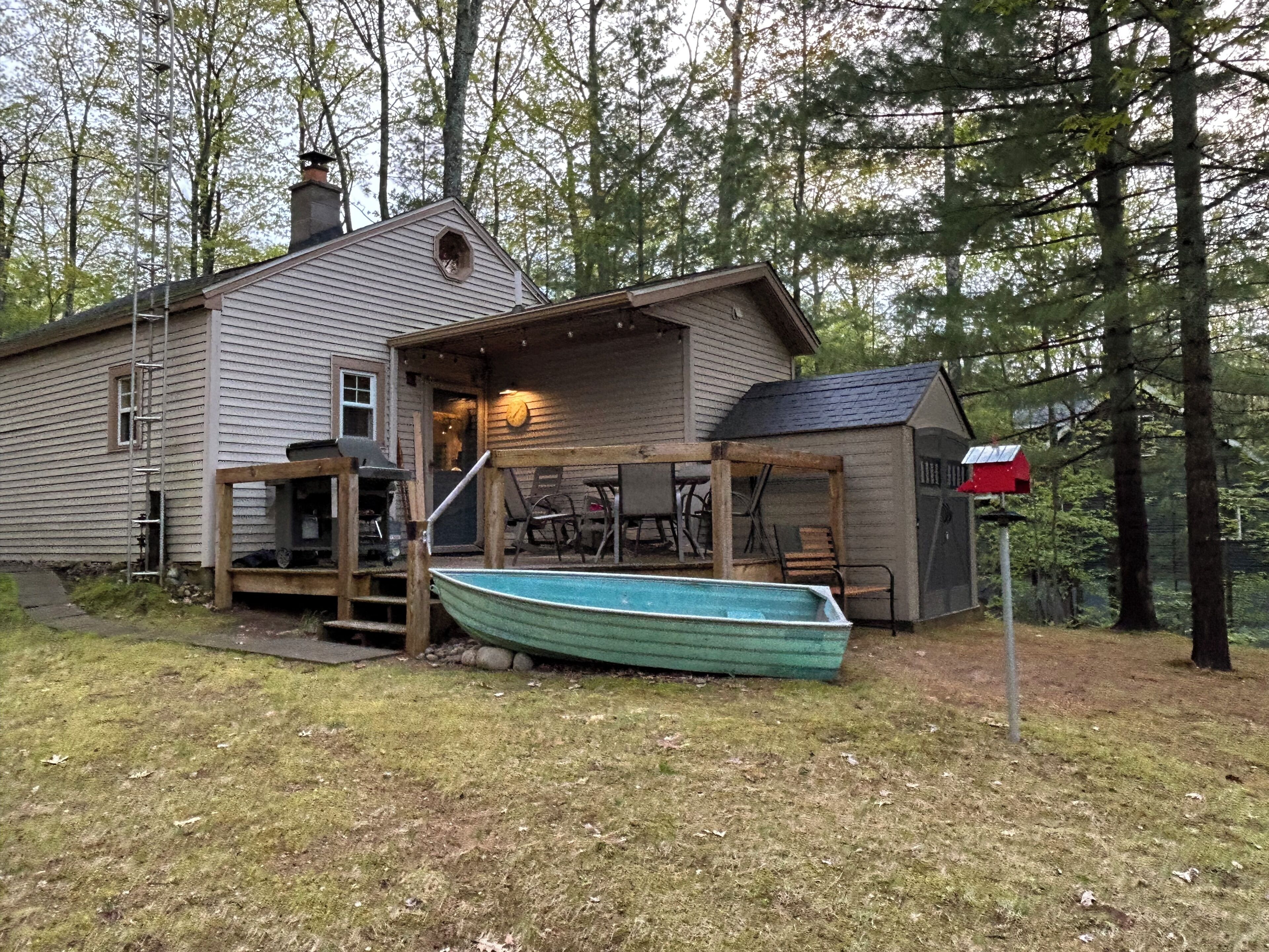 Une maison avec un bateau amarré devant, une véranda avec des chaises et une boîte aux lettres.
