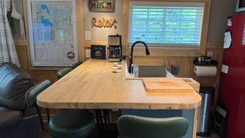 Une cuisine avec un îlot central en bois, des tabourets de bar, une machine à café et une carte accrochée au mur.