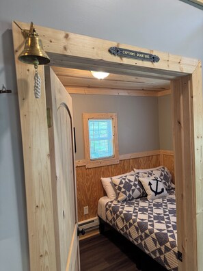 A cozy cabin-style room with a bed, a window, a wooden ceiling, and a bell.