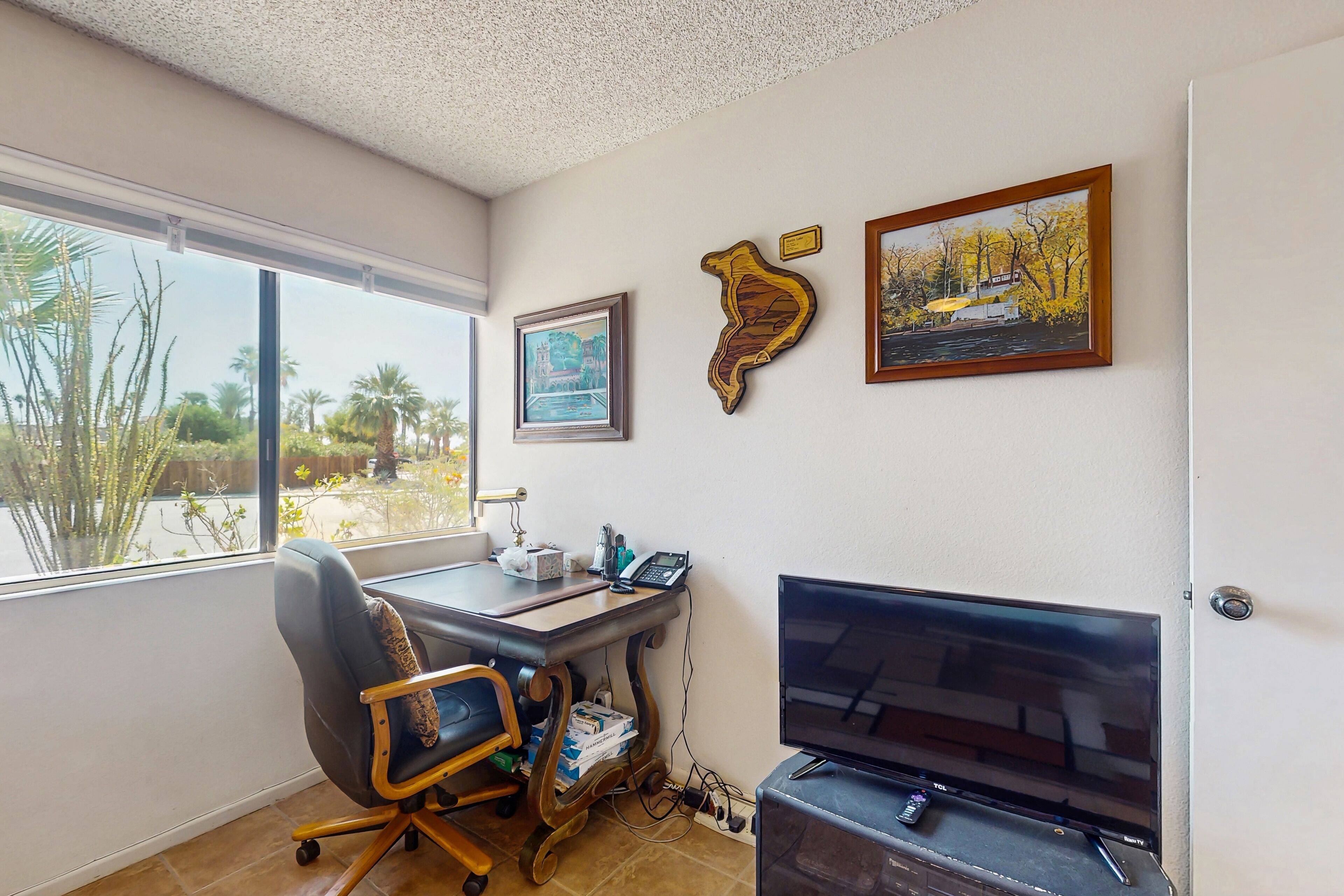 Una habitación con escritorio, silla, televisión y una obra de arte en la pared.