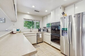 A modern kitchen with white cabinets, stainless steel appliances, and a window providing natural light. - Dog-friendly home w/private pool, patio, pool spa, and gas fireplace (Palm Springs)