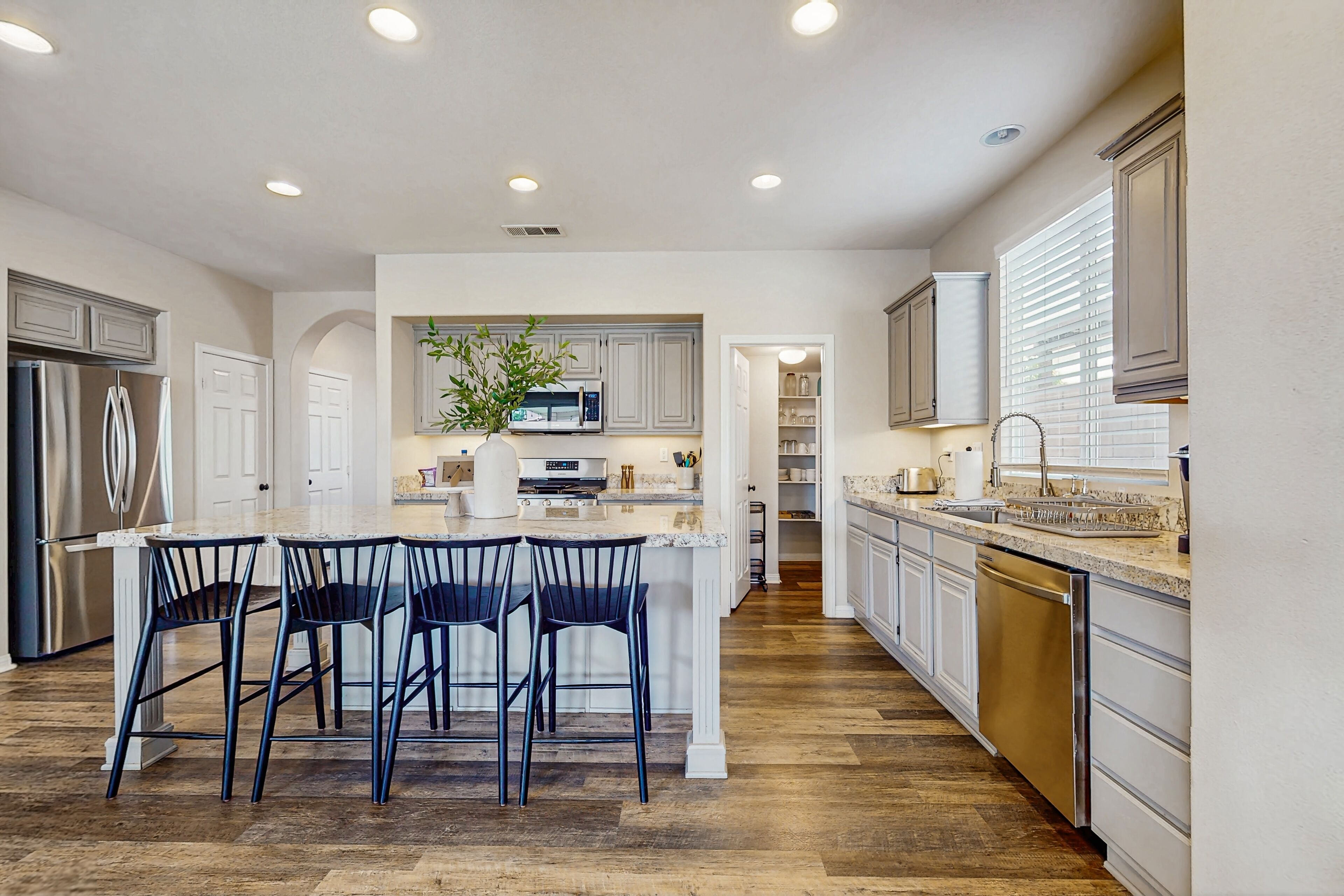 Una cocina moderna con una isla central, muebles blancos y un refrigerador de acero inoxidable.
